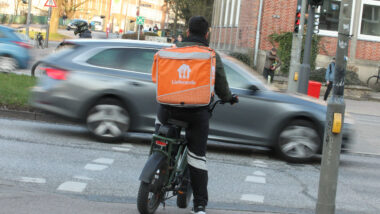 Ein Kurier vom Lieferdienst Lieferando steht mit seinem Fahrrad an einer roten Ampel.